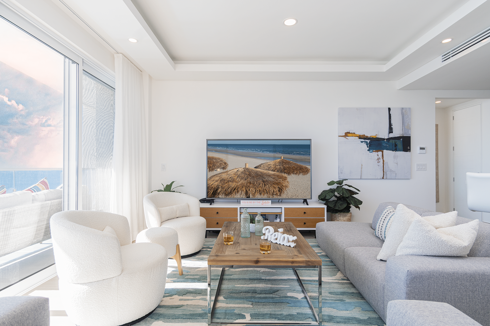 Living room with a couch, chairs, and a TV displaying a scenic beach